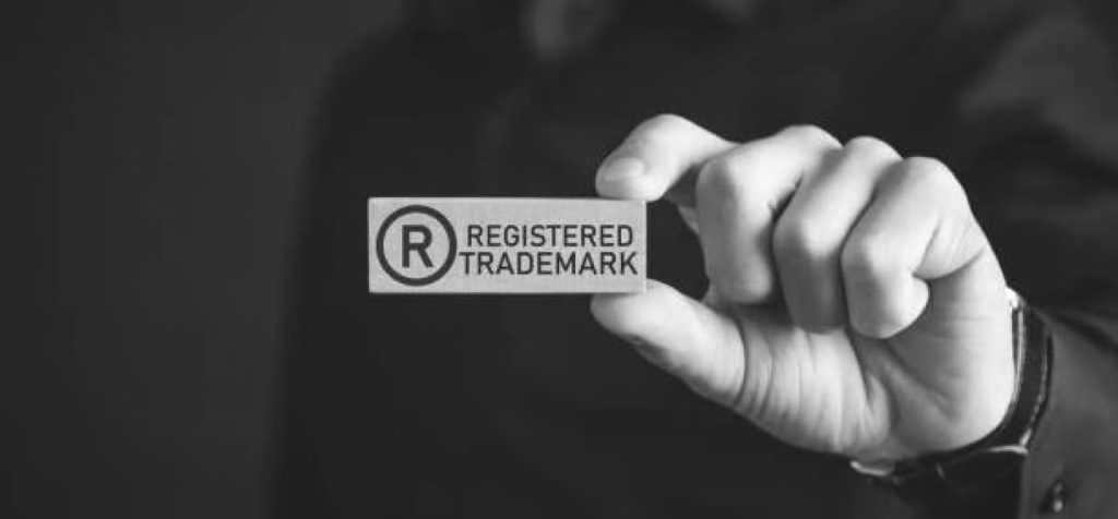 A person holds a card displaying the registered trademark symbol and the words "REGISTERED TRADEMARK" in black and white.