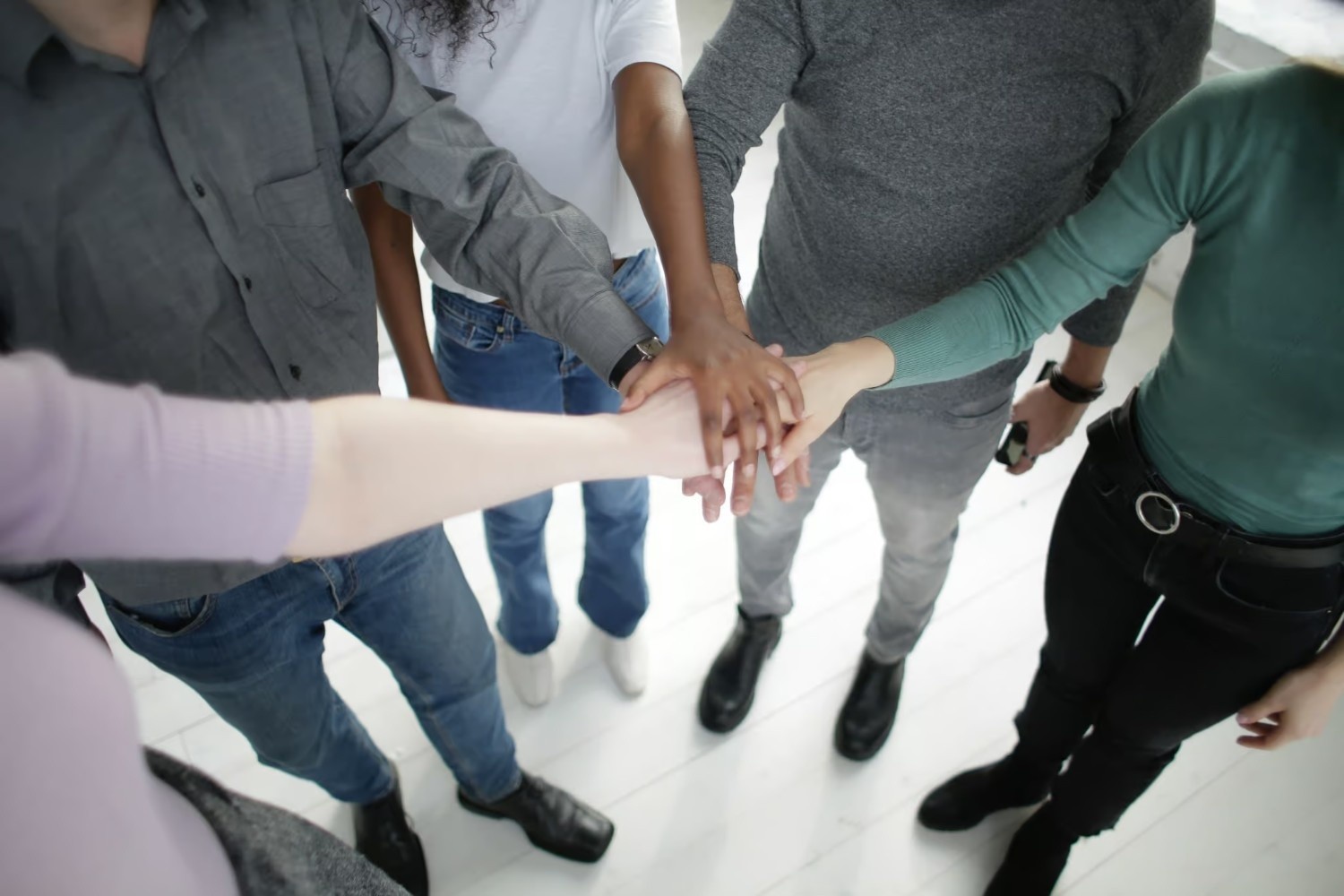 Five people standing in a circle place their hands together in the center, showing teamwork and unity.
