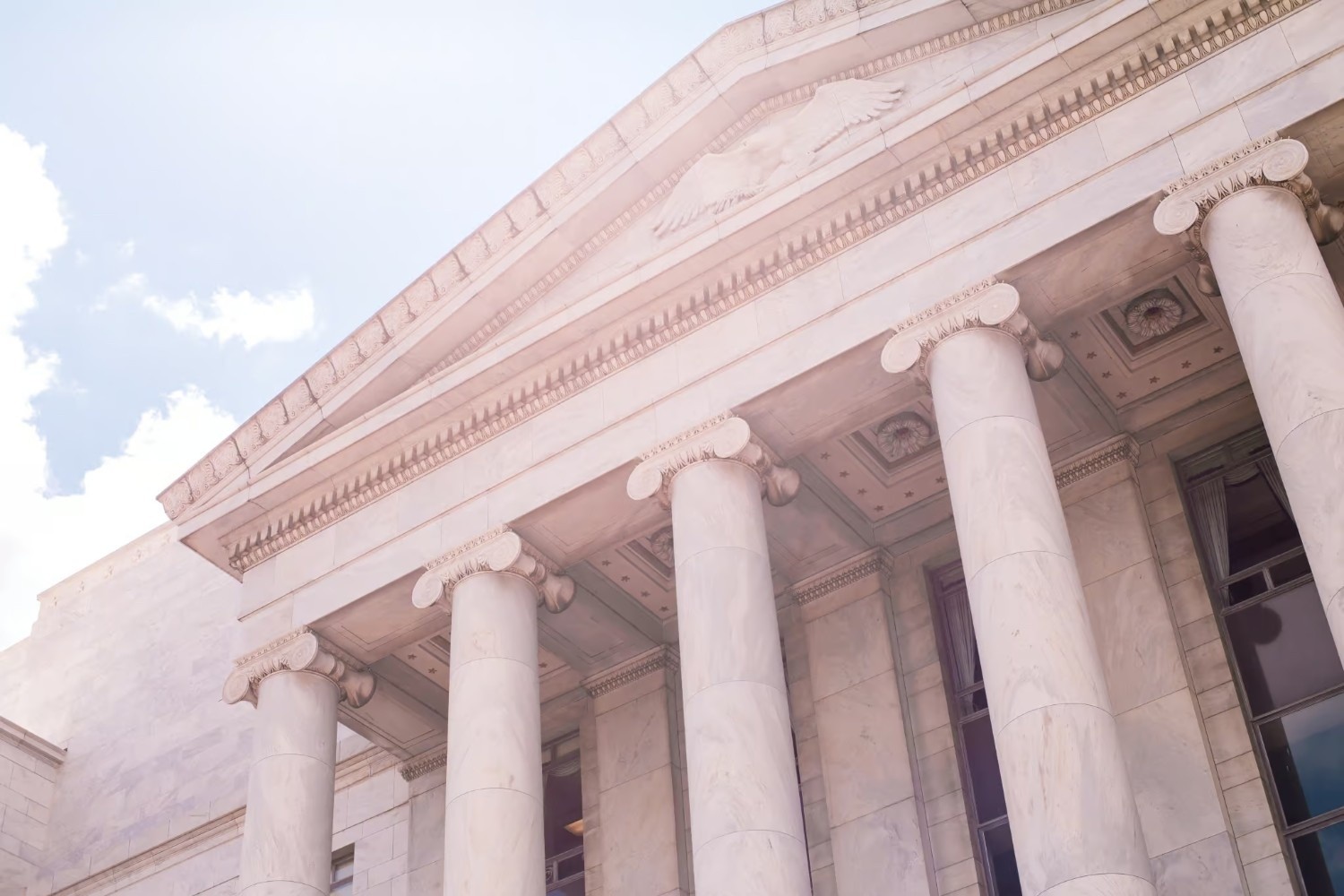 A neoclassical building with tall marble columns and an ornate pediment under a bright sky.